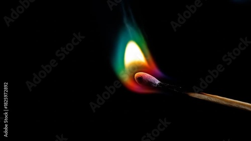 Burning matchstick with colorful flame against a black background