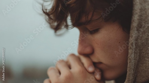 Close-up of a young boy's face, with his eyes closed and his hands clasped together in prayer. he appears to be deep in thought or contemplation.