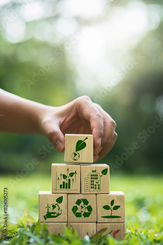 Hand stacking wooden blocks with symbols of sustainability and environmental conservation. This represents Corporate Social Responsibility (CSR) and the journey toward a green business future.