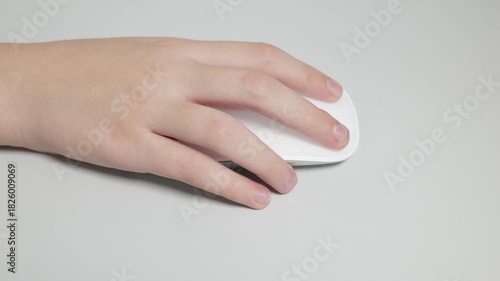 A close-up shot of a man's hand clicking and moving a sleek white wireless computer mouse on a gray office desk. The scene represents work, technology, and computing.
