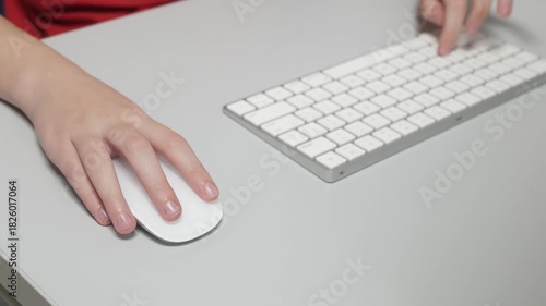 A wide shot showcasing both hands actively using a sleek white wireless mouse and keyboard on a gray office desk. The scene represents dual tasking, fast computing, and efficient modern work.