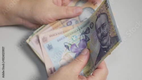 A close-up shot of hands carefully counting and fanning out Romanian Leu banknotes. The scene represents finance, banking, saving, payment, and currency exchange.