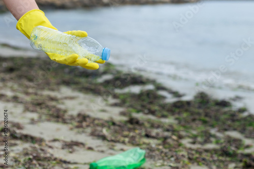 volunteer collecting plastic bottles on a polluted beach, highlighting ocean pollution, waste problem, environmental protection and coastal cleanup action.
