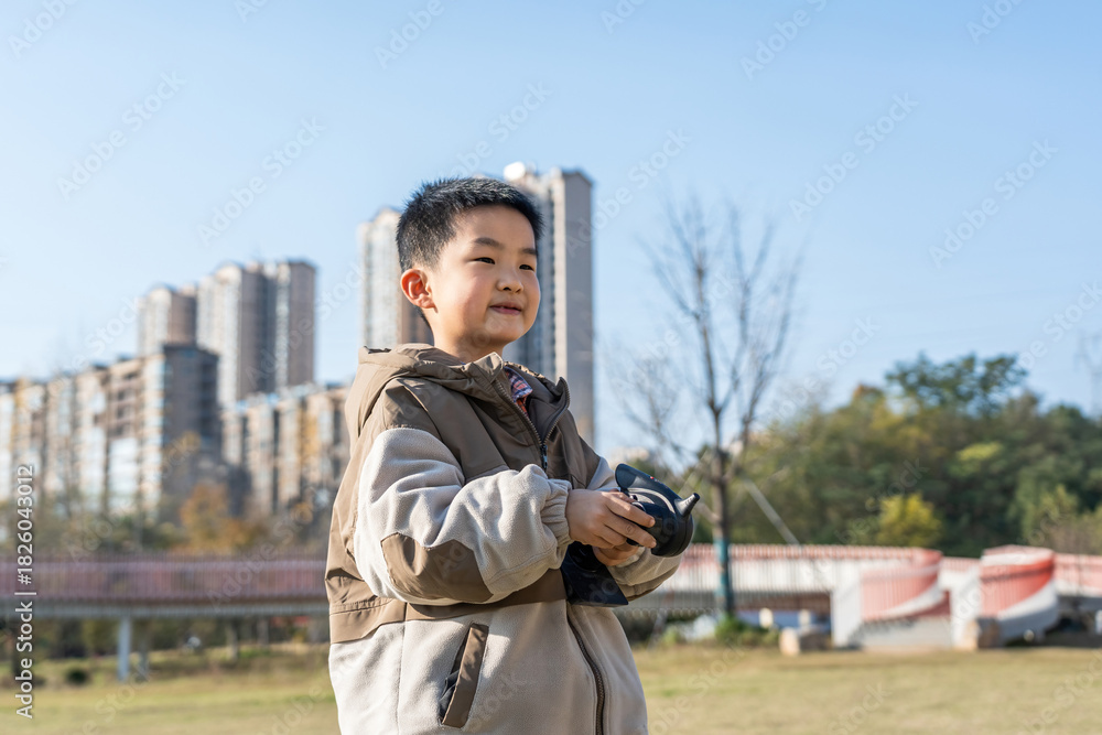 Fototapeta premium A young boy is holding a camera while standing outdoors in an urban area with buildings in the background.