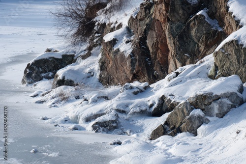 Rocky shoreline covered in snow and ice with frozen water in foreground image