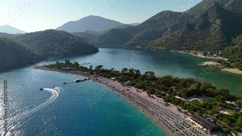 Aerial view of the famous Blue Lagoon in Oludeniz, Turkey, showing turquoise water, beach, people swimming, boats, and green mountains on a sunny summer day.