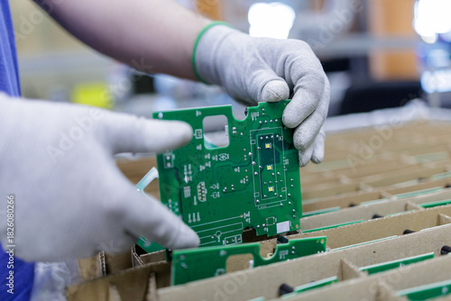Worker placing green printed circuit board into packaging tray at electronics factory