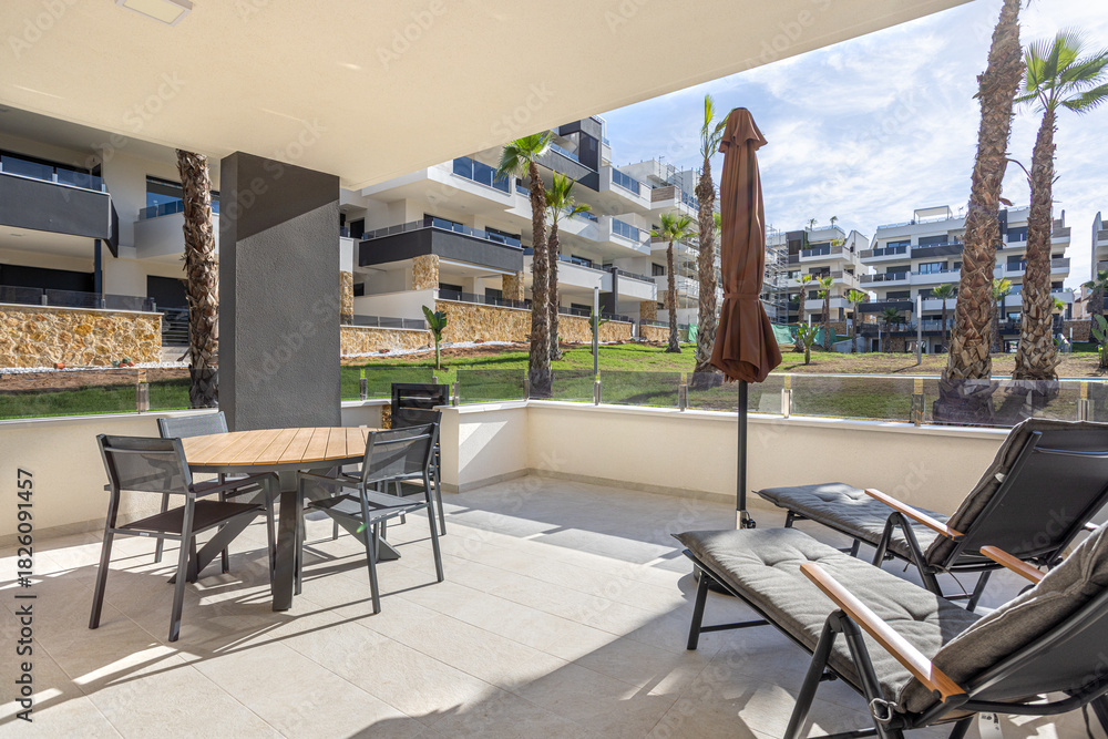 Naklejka premium Large sunny terrace with lounge chairs, dining table, and garden view