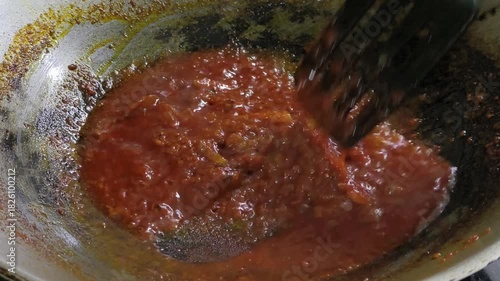 A chef is preparing sambal in a wok. This spicy relish is a commonly served dish essential to Malaysian cuisine.