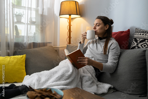 Woman relaxing at home, reading book and drinking coffee