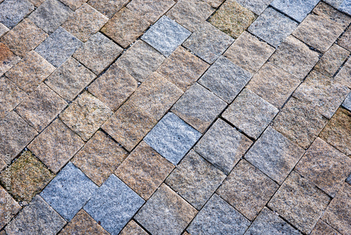 Fototapeta Naklejka Na Ścianę i Meble -  Close-up of textured stone pavement made of small square granite blocks arranged in an interlocking pattern.