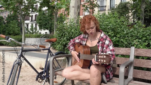 Young woman singing and playing guitar on a park bench