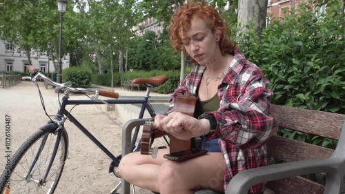 Young redhead woman tuning guitar in park