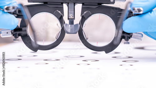 An optometrist wearing blue gloves measures visual acuity using special test glasses for lens selection. High quality photo