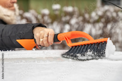 A woman clears snow from her car before leaving for work, clearing snow from a car with an orange soft brush, preparing a car for driving in winter,