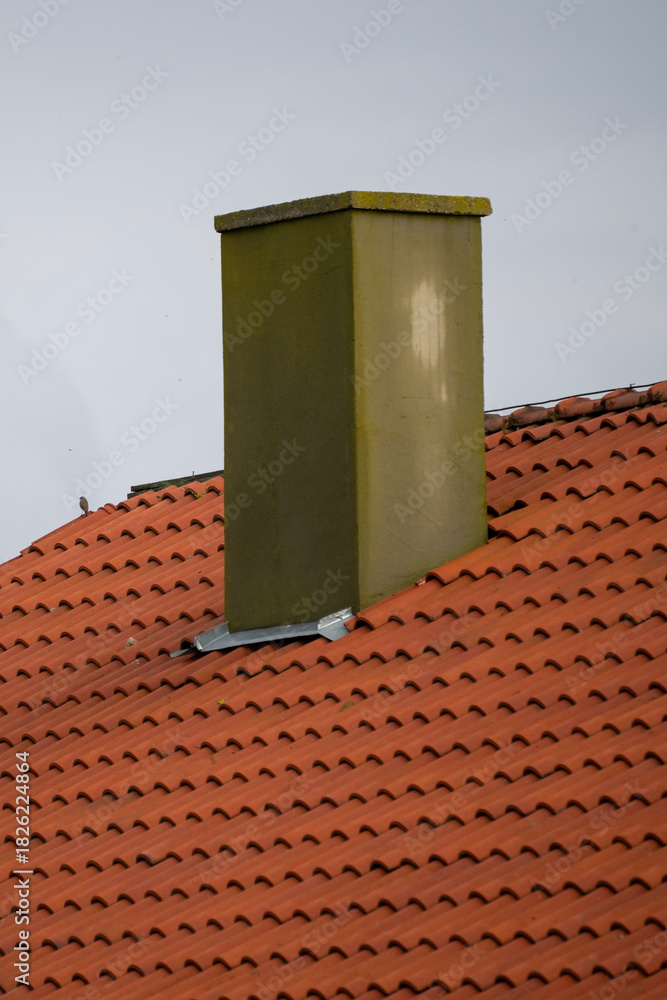 Naklejka premium A rectangular chimney rises from a red-tiled sloped roof, surrounded by metal flashing and weathered textures.