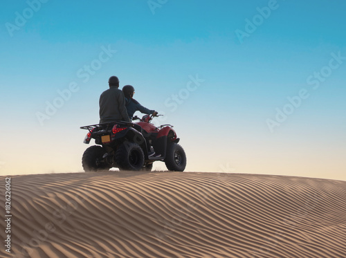 Fototapeta Naklejka Na Ścianę i Meble -  Two men on quad bike riding on sand dunes in desert during golden time.