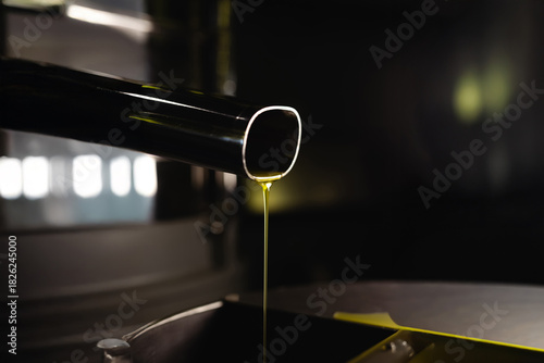 Fresh golden olive oil flowing from metal pipe after filtration. Final stage of EVO oil production in a modern oil mill.