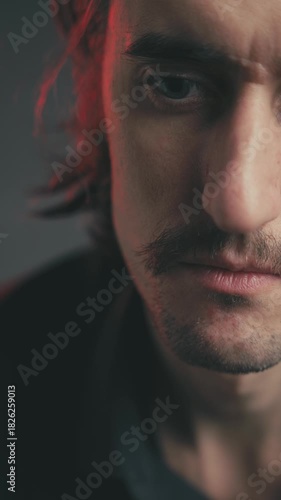 Dramatic close-up of a young attractive Slavic man with a mustache and long hair, showcasing sadness and pain through his serious expression in moody red lighting.