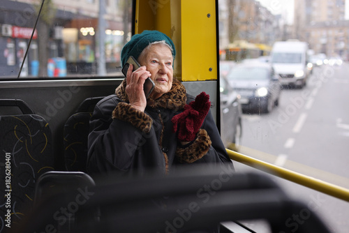 A senior woman is sitting on a bus, using her smartphone. She is traveling through the city, enjoying her journey in a relaxed manner.