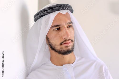A man wearing a white robe and a black turban is looking at the camera. He has a beard and a mustache