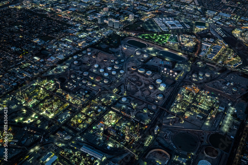 Aerial night view of industrial refinery complex and surrounding urban area in Los Angeles County, California, showing illuminated tanks, factories, and infrastructure
