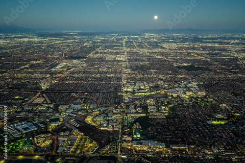 Aerial view of illuminated Los Angeles grid at night under a full moon, showing vast urban sprawl, streets, and city lights extending to the horizon across Southern California