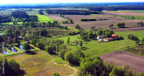 Aerial view of rural agricultural landscape featuring farm buildings, cultivated fields, forests, and aquaculture fish ponds