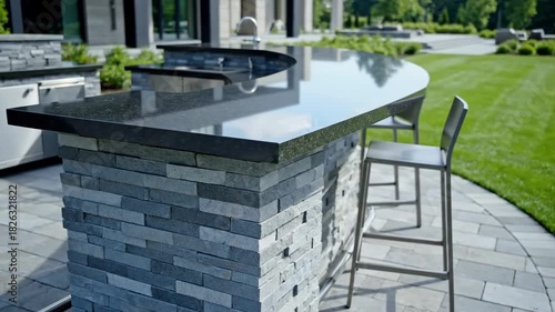 Outdoor stone bar and granite countertop in a modern backyard setting with lush green lawn