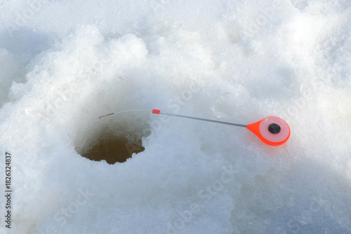 Red fishing float on rod bobbing near ice fishing hole during winter fishing. Outdoor winter activity hobby leisure recreation kind of sport. Competition in catching fish.