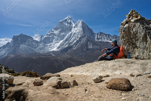 Hiker resting by cairn viewing Ama Dablam peak on Everest Trek, Nepal