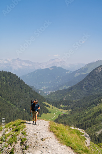 Hiker walking down steep alpine trail overlooking valley, French Alps