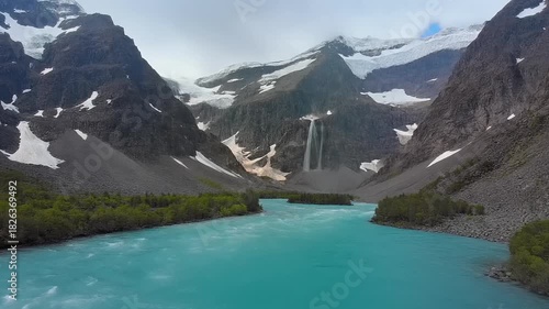 Majestic Mountain Valley with Turquoise Glacial River and Distant Waterfall,Snowy Peaks and Lush Green Forest in Wilderness Landscape