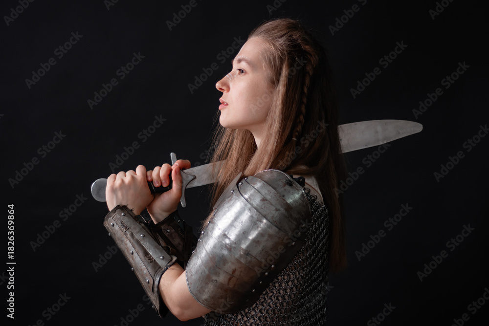 Obraz premium Portrait of a young woman, fantasy warrior in armor with a sword in her hands isolated on a dark background.