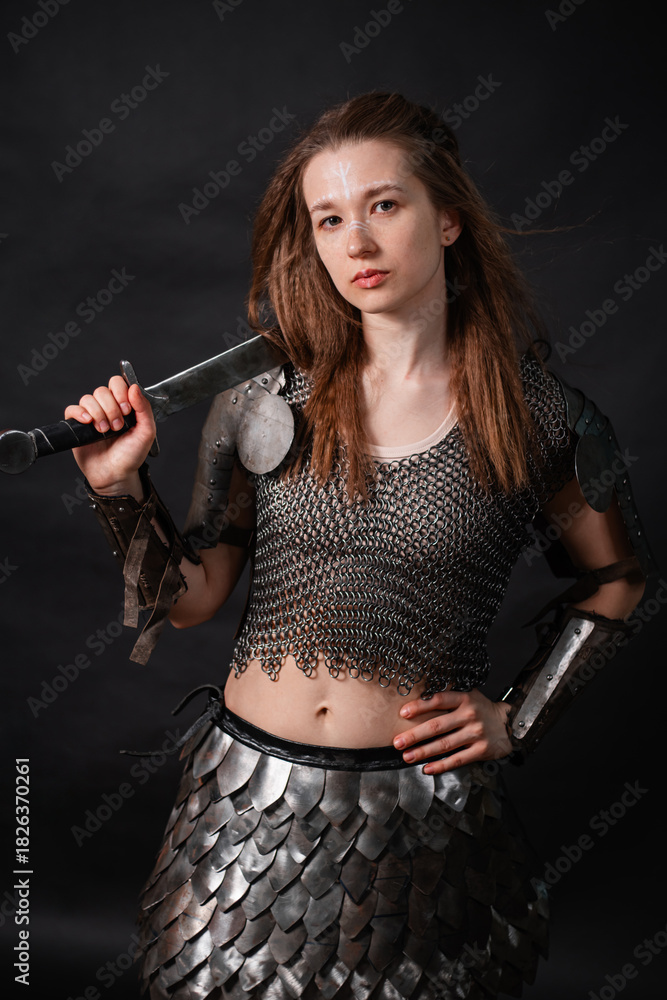 Obraz premium Portrait of a young woman, fantasy warrior in armor with a sword in her hands isolated on a dark background.