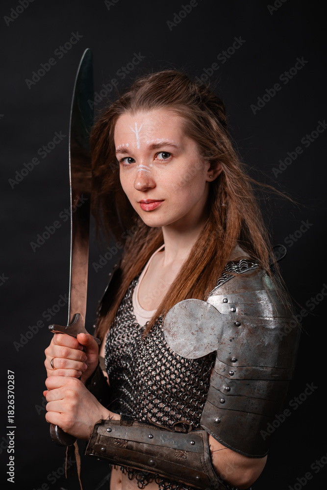 Naklejka premium Portrait of a young woman, fantasy warrior in armor with a sword in her hands isolated on a dark background.
