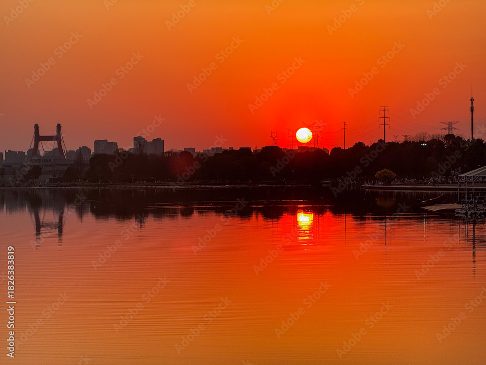 Fototapeta premium Dramatic Orange Sunset Over City Skyline and Bridge Reflected in Calm Lake Water, Hangzhou, China.