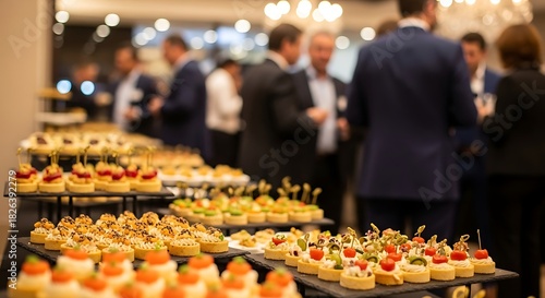 Catering service offering a variety of gourmet canaps and appetizers displayed on a buffet table during a corporate event or reception with blurred business people in background