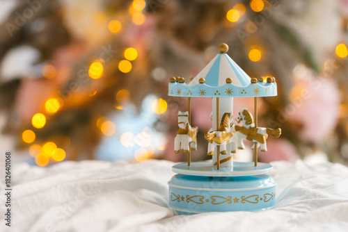 Christmas decor, cute vintage style blue carousel toy placed on soft fabric with warm golden lights bokeh on background, magical and nostalgic mood, winter holiday feeling and aesthetic atmosphere.