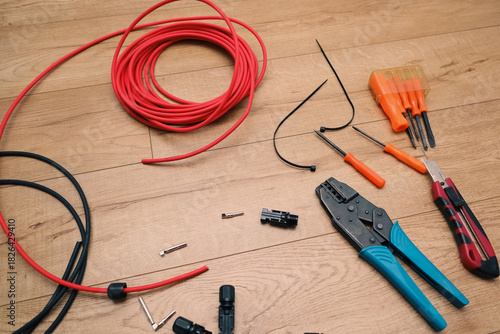 Solar panel wiring tools. Wire, connectors, crimping pliers on wooden floor.