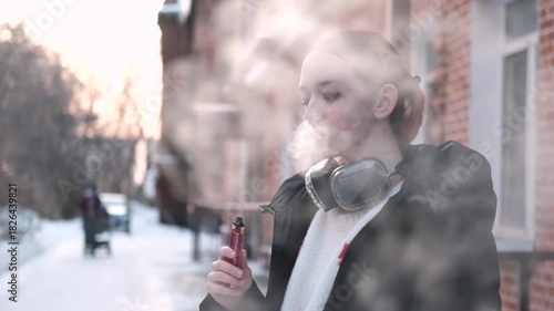 Teen vaper. A young girl smokes an electronic cigarette outside in winter. Close-up.