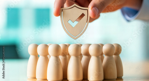 Hand places a wooden shield with a checkmark over a group of wooden figures, symbolizing security and care