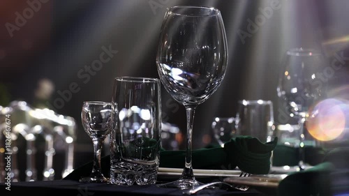 Luxury wedding banquet decoration in hall restaurant. Festive table setting with flower arrangement, large candlesticks with candle, chairs for guests, soft moving lights rays. Dinner table reception
