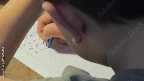 close up child hand forming lowercase a on lined notebook slow careful movement learning to write letters school preparation Concept of concentration skill building and early writing growth