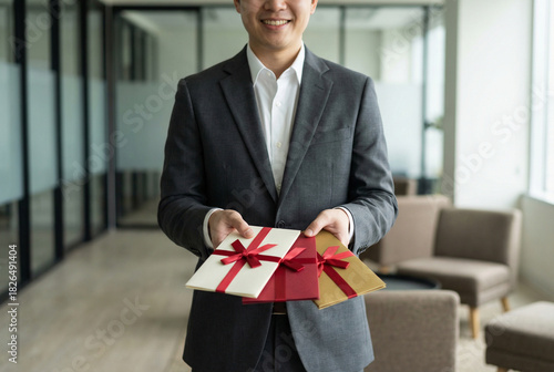 Businessman holding festive gift envelopes with red ribbons, corporate reward bonus and employee appreciation.