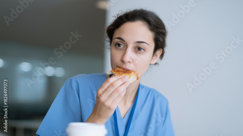 Nurse woman blue uniform eating pizza break room tired overworked healthcare hospital quick meal stress fatigue young adult professional medical staff lunch snack sitting indoors fast food