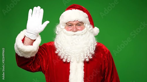 Santa Claus in a red suit and white beard waves, green background