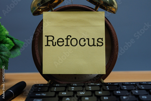 A yellow sticky note with the word “Refocus” on a clock face at a work desk, symbolizing a simple wellness concept of mindful breaks and regaining concentration.