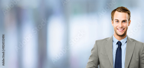 Portrait - happy smile confident business man in grey suit jacket, blue shirt, tie, against blurred office background. Businessman, bank manager, lawyer, teacher. Banner image with free ad text space