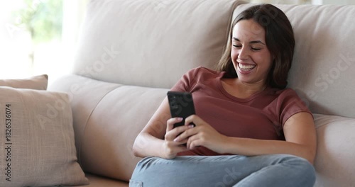 Happy woman on a couch using smart phone and laughing